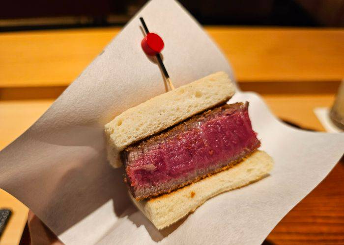 A thick wagyu beef katsu sando; a premium cut of wagyu beef between two lightly toasted slices of bread.